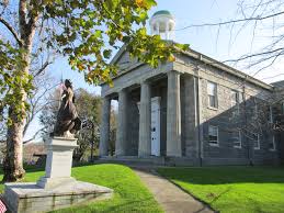 They grey stone facade of the Barnstable County Courthouse with four columns and statue on front lawn